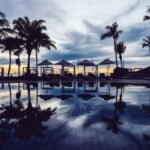 Sunset view of a luxurious poolside with palm trees, sun loungers, and umbrellas, showcasing serenity and elegance, perfect for the 5 best secret stays in California.