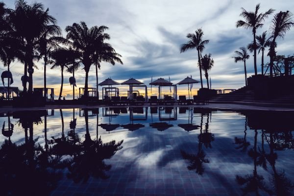 Sunset view of a luxurious poolside with palm trees, sun loungers, and umbrellas, showcasing serenity and elegance, perfect for the 5 best secret stays in California.